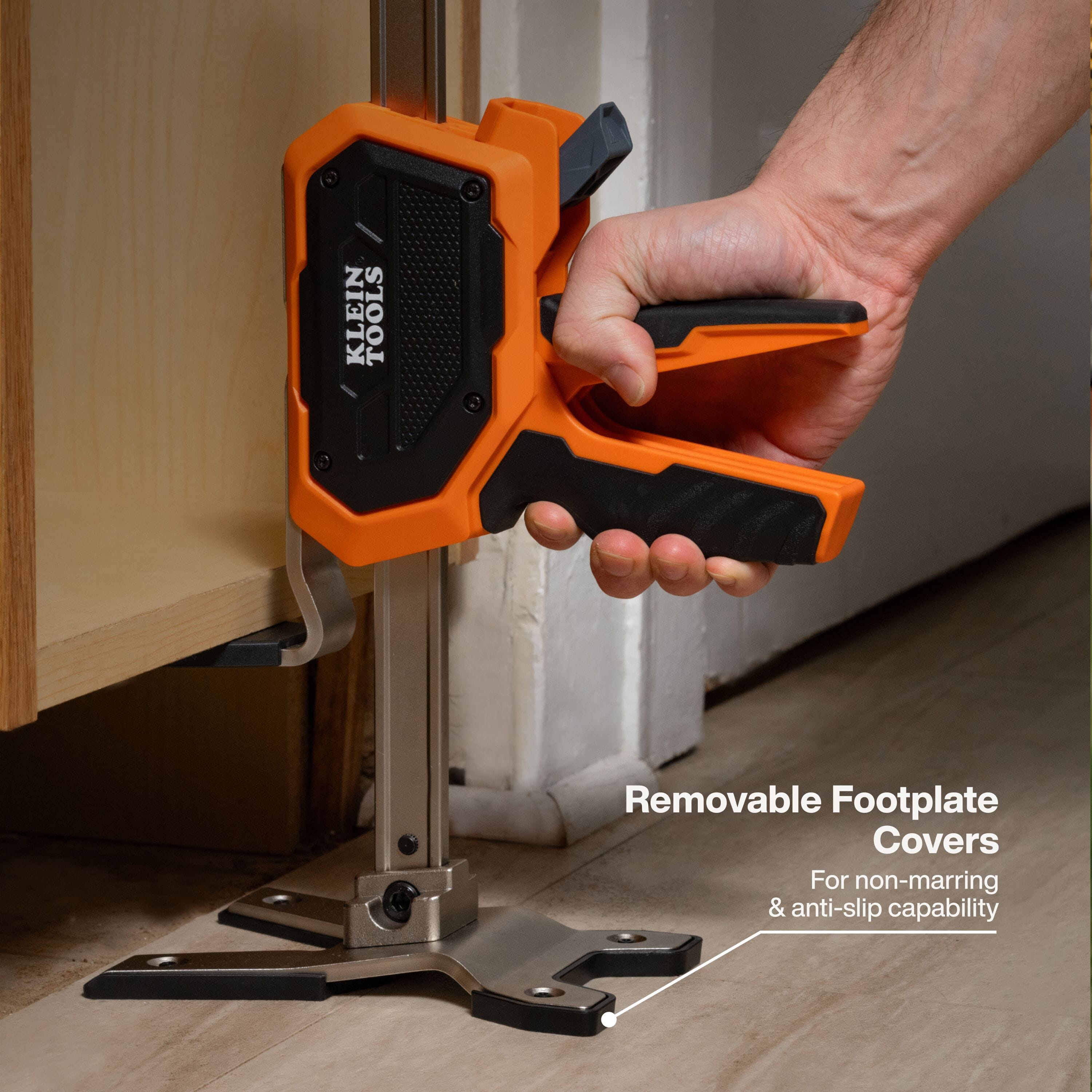 Close-up detail showing a tradesperson using the construction jack to level a kitchen cabinet, highlighting the removable non-marring footplate covers that provide anti-slip stability and protect finished surfaces.