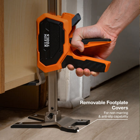 Close-up detail showing a tradesperson using the construction jack to level a kitchen cabinet, highlighting the removable non-marring footplate covers that provide anti-slip stability and protect finished surfaces.
