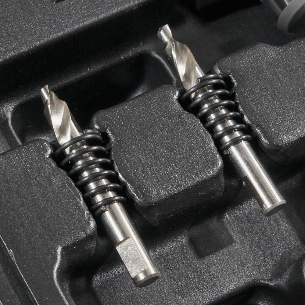 A close-up showing the two extra pilot bits with ejection springs resting in their molded slots in the carrying case.