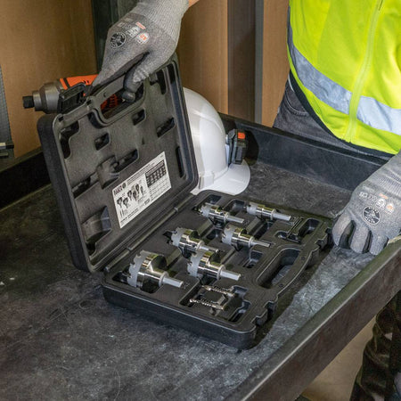 A worker in gloves opens the Klein carbide hole cutter kit on a utility cart, revealing all six cutters and pilot bits.