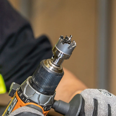 A close-up of a Klein carbide hole cutter with its ejection spring, chucked into a drill and ready for use.