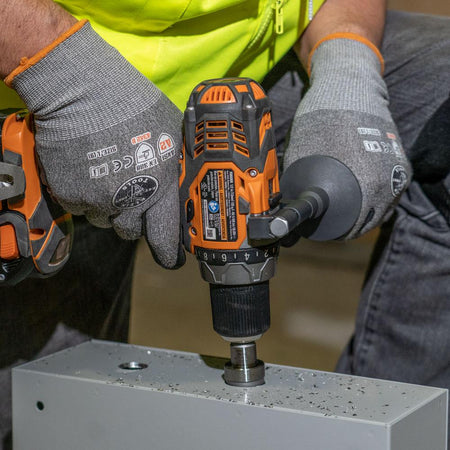 A worker wearing gloves uses a drill with a Klein pilot bit to start a hole in a metal electrical box.