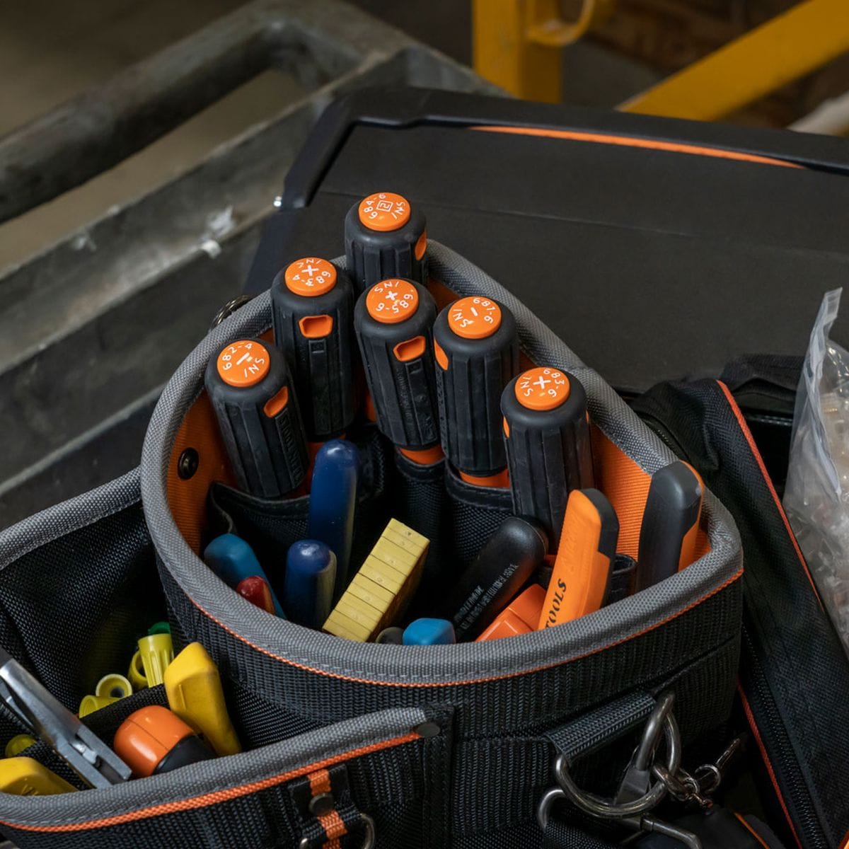 An assortment of Klein Tools 1000V safety-insulated screwdrivers stored systematically inside a rugged black canvas contractor tool pouch with orange piping lines, displaying high-visibility orange handle butt caps stamped with explicit white alphanumeric Tip-Ident drive geometry icons for quick selector access.