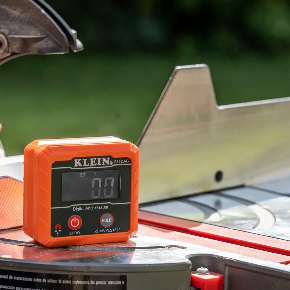 The digital angle gauge resting on the flat metal surface of a table saw, displaying 0.0 degrees to set a reference plane.