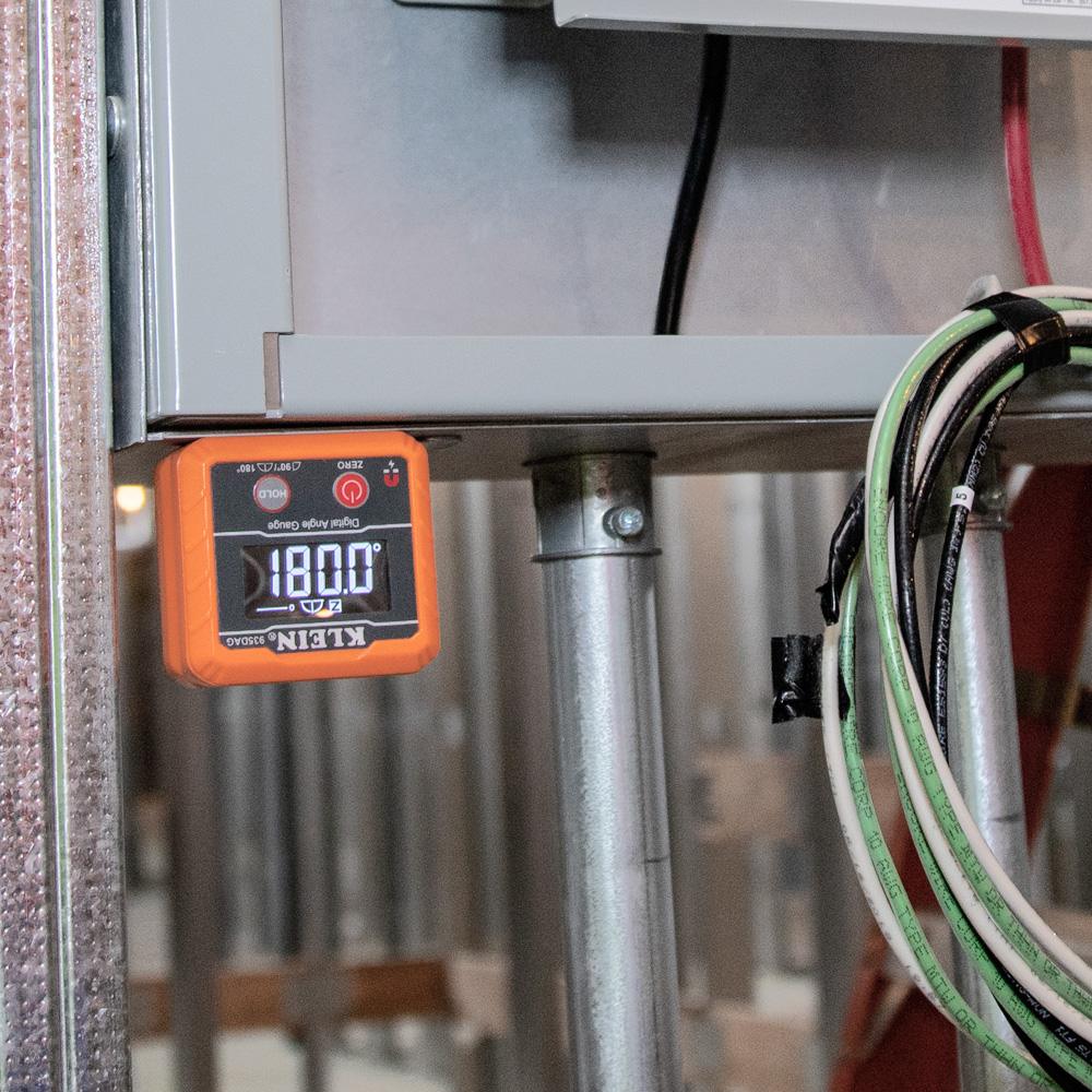 The angle gauge attached upside down to the bottom of a metal electrical box, displaying a reading of 180.0 degrees.