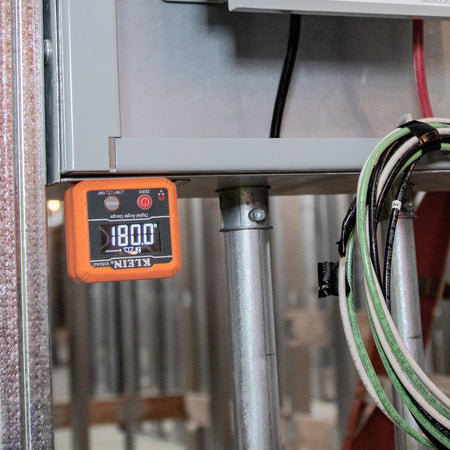 The angle gauge attached upside down to the bottom of a metal electrical box, displaying a reading of 180.0 degrees.