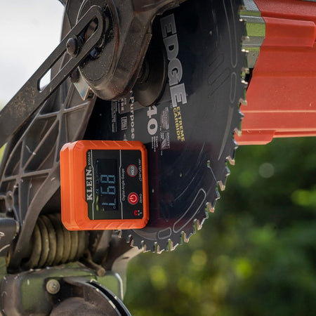 The digital angle gauge attached magnetically to the flat side of a miter saw blade, displaying a reading of 89.7 degrees for calibration.
