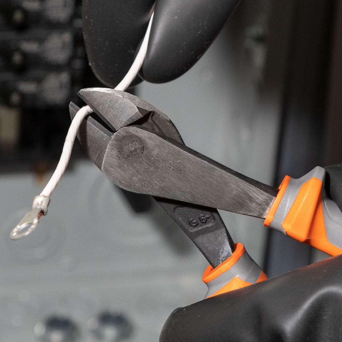 An operator wearing thick black rubber protective safety gloves uses a pair of Klein Tools 1000V insulated high-leverage diagonal cutting pliers to snip through a solid copper electrical cable wire, showcasing the heavy cutting jaw edge performance and high-dielectric handle material under hot line work conditions.