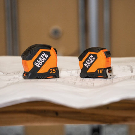 Comparison shot showing a 25-foot and a 16-foot Klein Tools compact tape measure side-by-side on top of architectural blueprints.