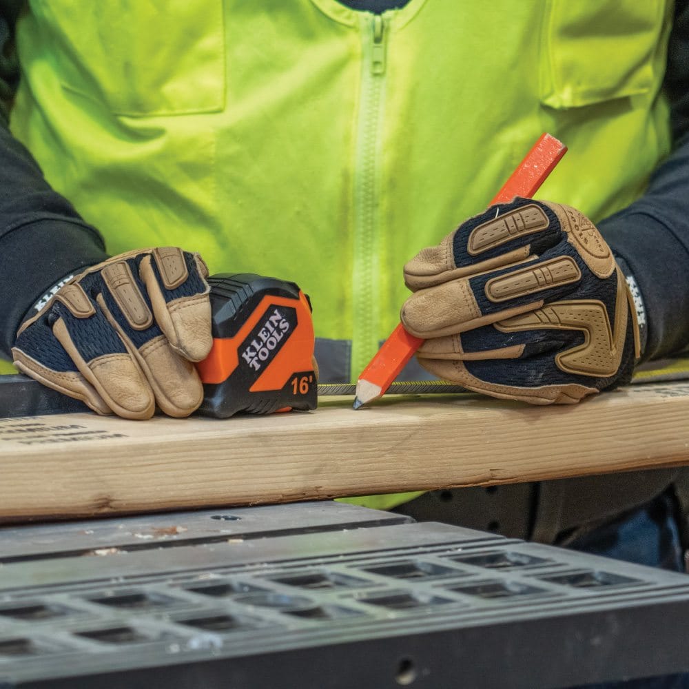 A technician using the Klein Tools 16-foot tape measure and a carpenter's pencil to mark a piece of lumber for cutting.