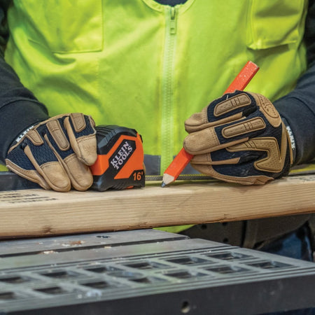 A technician using the Klein Tools 16-foot tape measure and a carpenter's pencil to mark a piece of lumber for cutting.