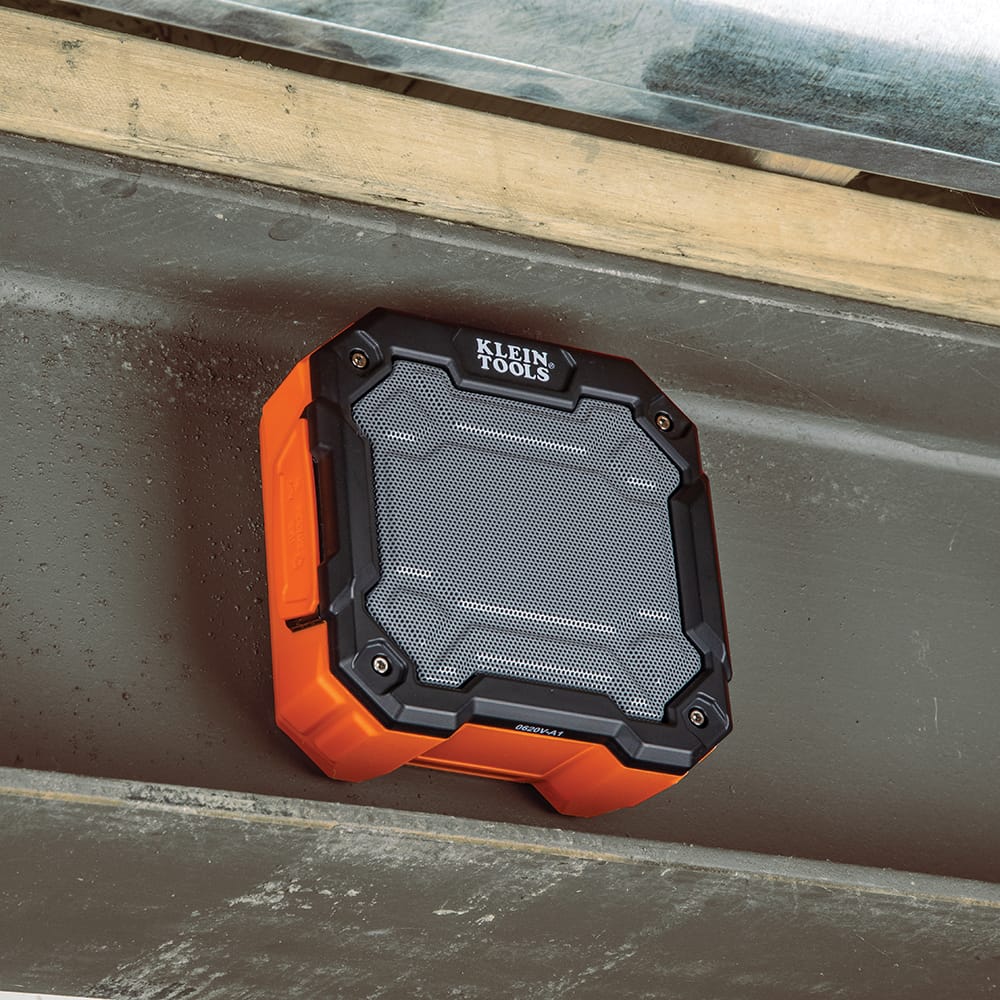Klein Tools AEPJS3 drop-proof jobsite speaker securely attached underneath a large steel I-beam utilizing its powerful embedded magnetic mount.