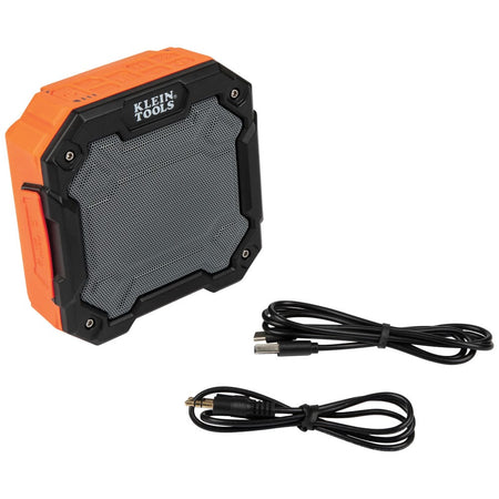 Klein Tools AEPJS3 IP54 water-resistant portable Bluetooth speaker displayed next to its included USB-A to USB-C charging cable and 3.5mm auxiliary cable.