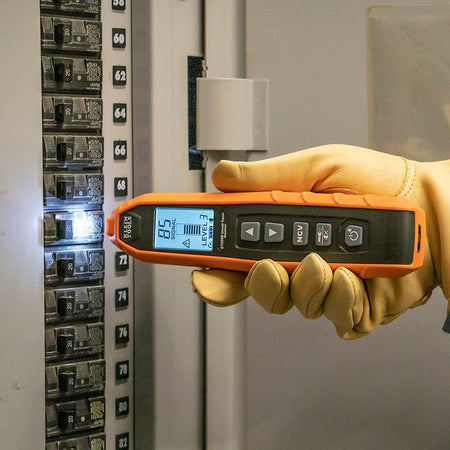 Person using Klein Tools digital tester on a circuit breaker panel, with screen showing “85”, “Level 3”, and “NCV” for voltage and signal strength.