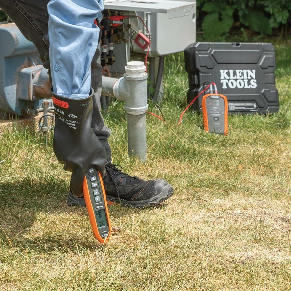 Technician using Klein Tools electrical tester outdoors near an open electrical panel, with protective gear and carrying case visible on grassy surface.