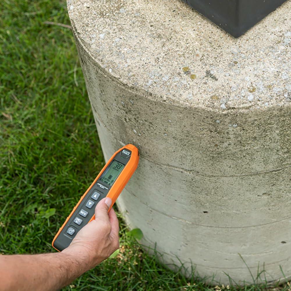 Person using handheld Klein Tools device to measure a cylindrical concrete structure, with screen displaying “20 mm” for depth or thickness reading.