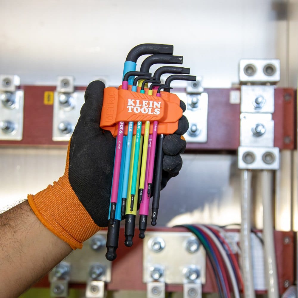 Detail shot of the metric portion of the Klein Tools BLS18 set held in front of an electrical panel, emphasizing the industrial-strength steel construction and color-coded organization.