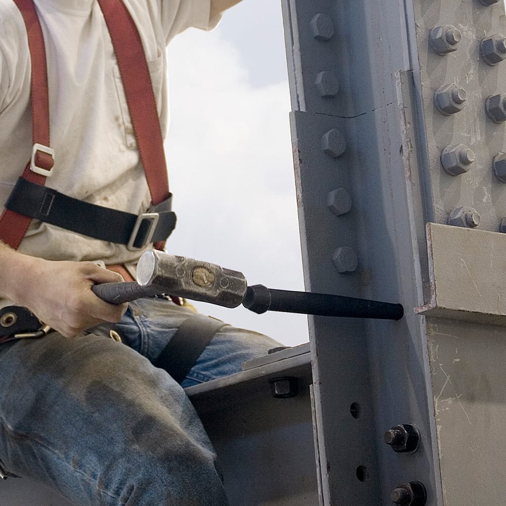 Ironworker using a hammer to strike the Klein 3255 broad-head bull pin to align misaligned bolt holes on a structural steel I-beam.