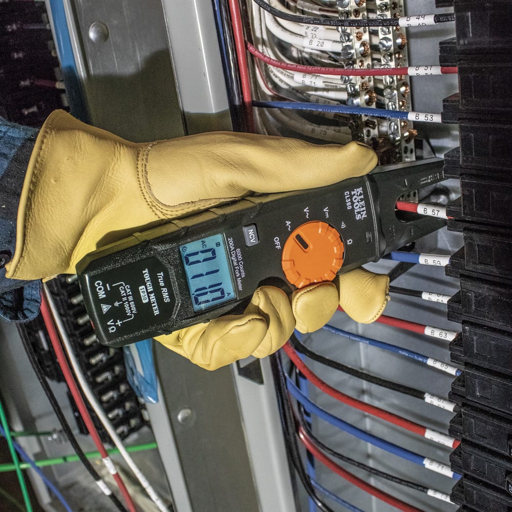 Action shot of a professional electrician using the Klein Tools CL360 Digital Open Jaw Fork Meter to measure AC current on a single conductor within a high-density breaker panel. The technician is wearing protective leather gloves, and the meter's backlit display clearly shows a live reading of 1.10 Amps, demonstrating the tool's precision in tight workspaces.