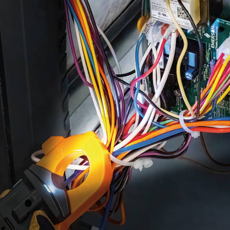 Action shot showing a professional using the CL445 clamp meter to verify voltage at a standard residential outlet. The technician, wearing protective gloves, uses the right-angle test leads to monitor real-time electrical data on the meter's backlit digital display.