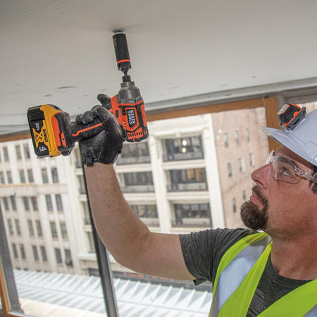 Electrician using a Klein coaxial 12-point spring-loaded socket on an impact driver to fasten overhead ceiling hardware hands-free.