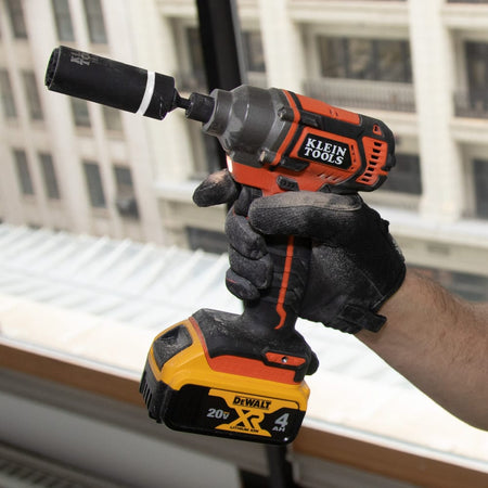 Worker holding a cordless impact driver fitted with a Klein 32mm by 27mm coaxial socket to demonstrate elevated overhead fastening.