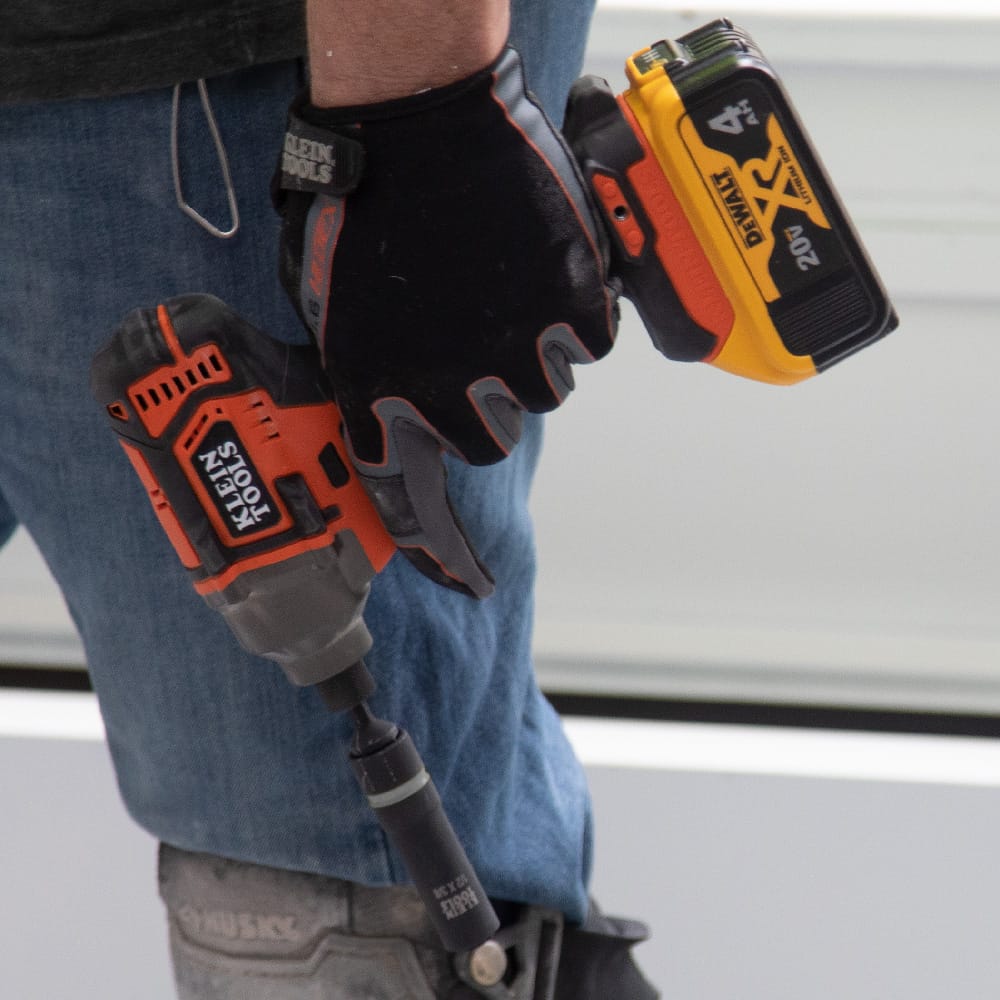 Gloved contractor carrying a 1/2-inch impact driver fitted with a Klein coaxial metric socket for transport around a jobsite.