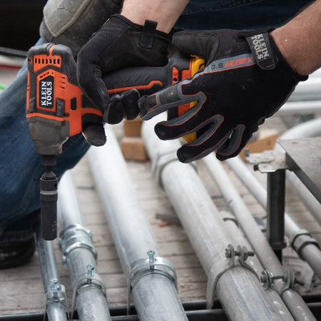Technician using a Klein coaxial 12-point socket on an impact driver to secure metal conduit support hardware on a jobsite floor.
