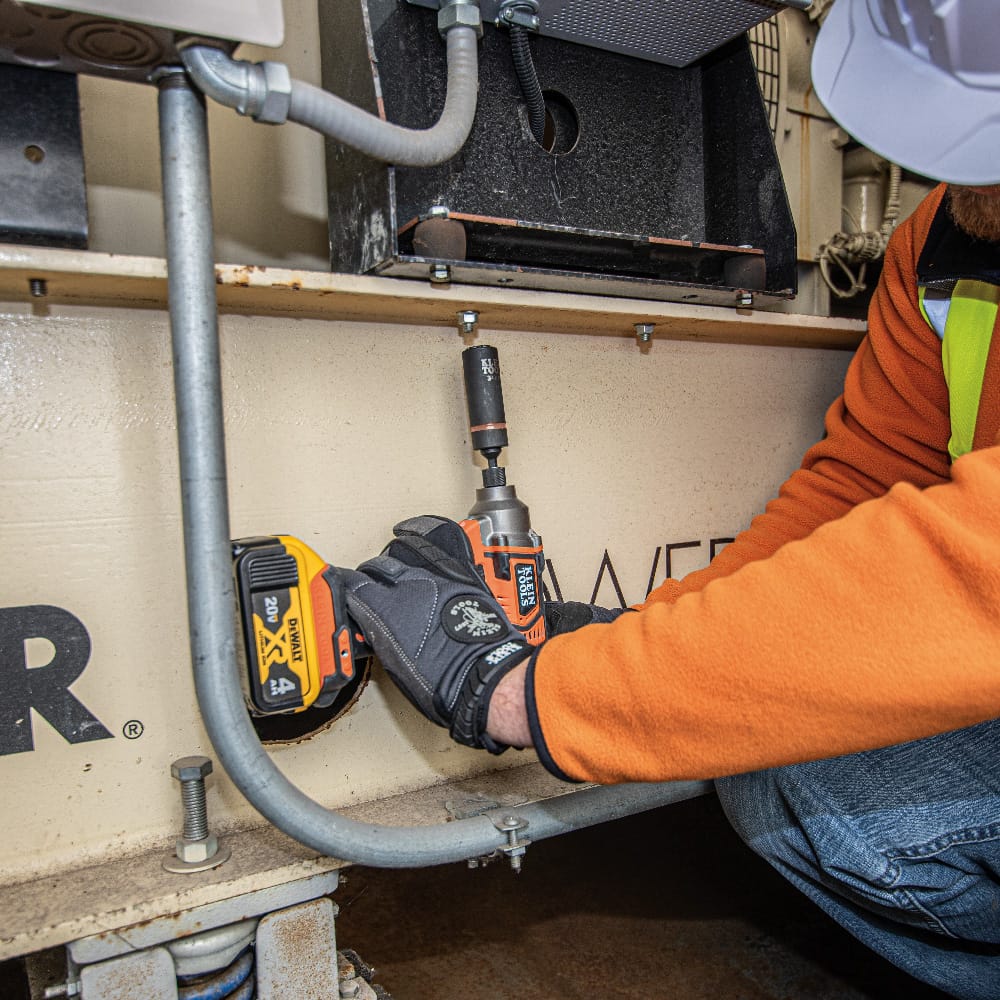 Maintenance worker operating a 1/2-inch impact wrench fitted with a Klein coaxial metric socket to tighten industrial equipment frame bolts.
