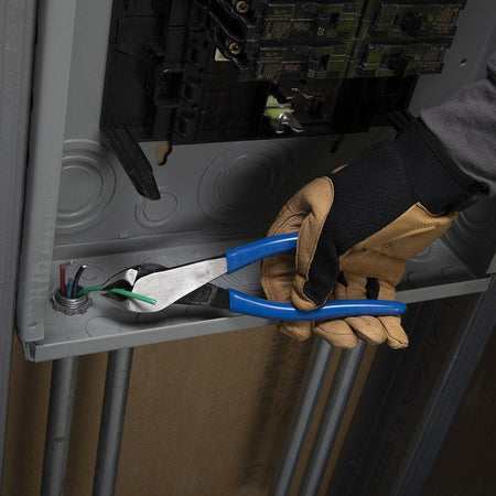 A tradesperson using the Klein D2000-48 heavy-duty diagonal cutters to trim a green grounding wire within a residential electrical service panel, highlighting the tool's precision in complex wiring environments.
