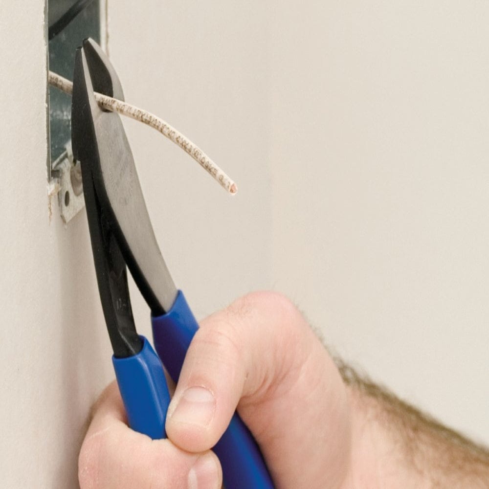 A close-up action photograph of a professional using Klein D2000-48 angled head diagonal cutters to precisely trim a white electrical wire protruding from a wall-mounted metal junction box.