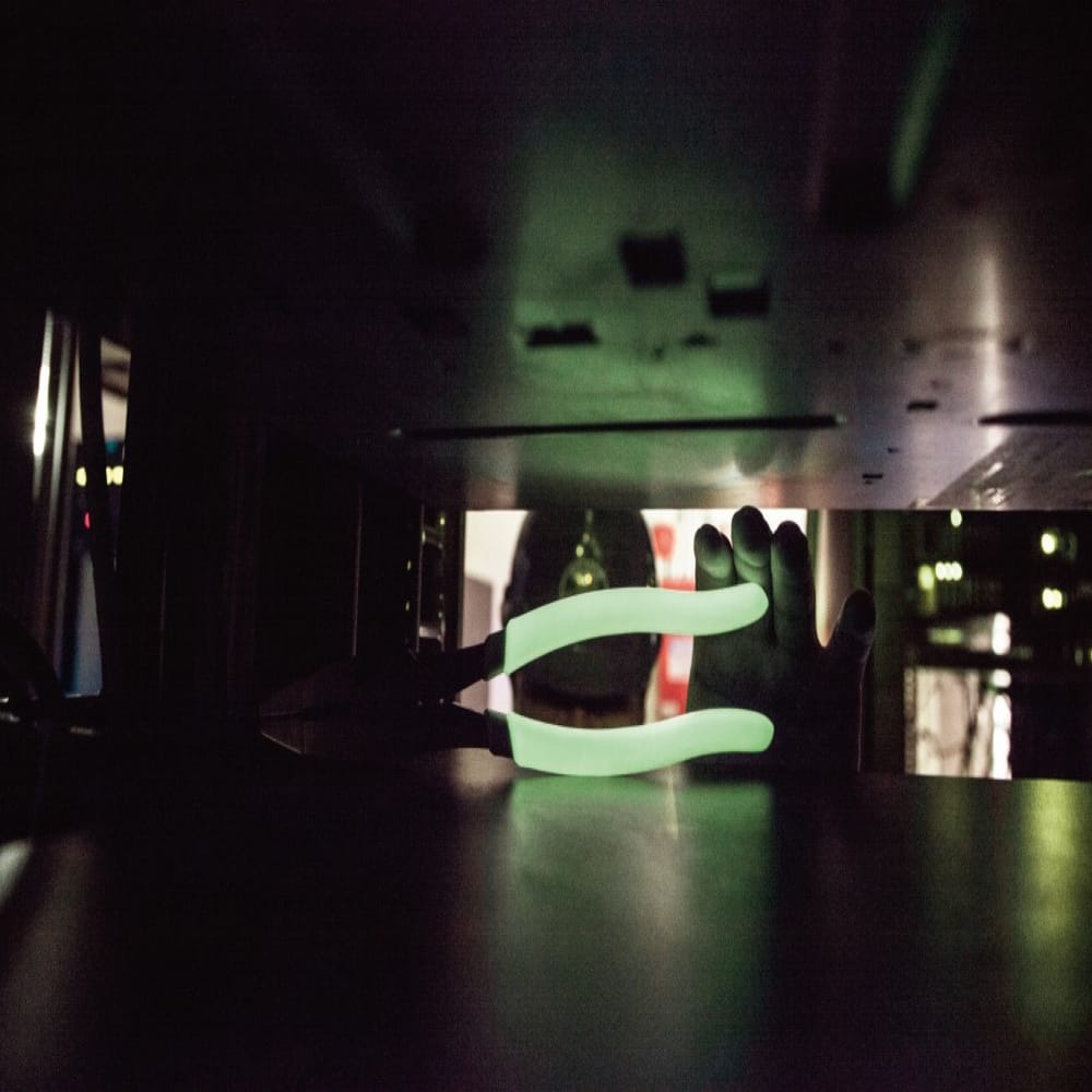 Glow-in-the-dark handles on diagonal cutting pliers illuminated inside a dark crawl space to provide instant tool visibility for electrical work.