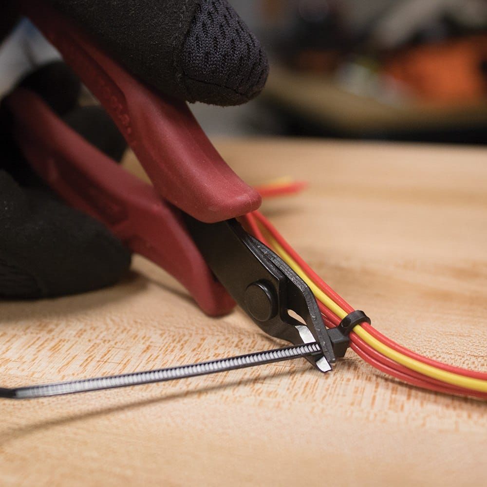 Action shot showing a person using the flush cutter to precisely trim the excess tail of a black zip tie, demonstrating the flat and smooth finish left by the tool.
