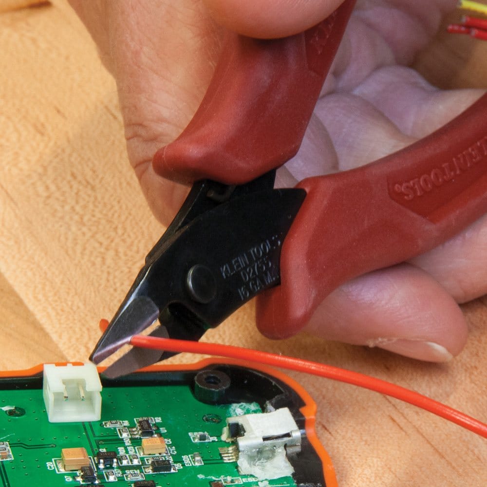 A technician using the D2755 flush cutter to snip small electrical wires inside a dense control panel, highlighting the tool's ability to reach into confined spaces.