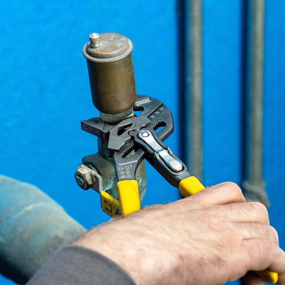 Top-down view of a professional using a Klein Tools adjustable plier wrench to maintain a plumbing fixture, highlighting the tool's precision and comfort-grip handles.