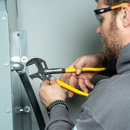 An electrician using the 7-inch plier wrench from the D53002KIT to secure a conduit elbow into an electrical panel, showcasing the tool's high torque and precision in tight spaces.