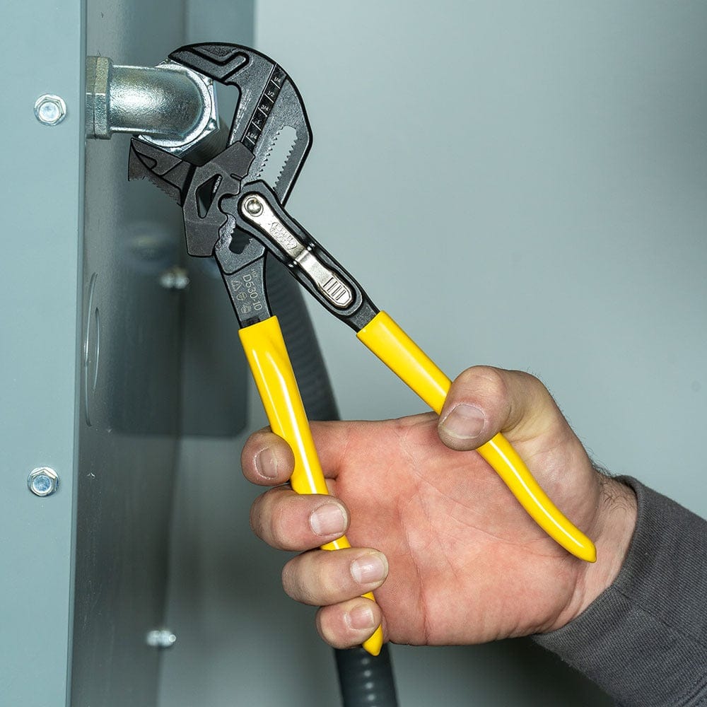 A close-up action shot of a professional using the 10-inch Klein Tools plier wrench on a large hex nut, demonstrating the high leverage and secure grip provided by the forged steel construction.