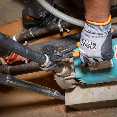 An industrial worker using the 10-inch Klein Tools compact plier wrench to tighten a large hex nut on a blue water pump system.
