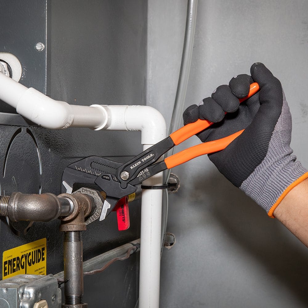 Technician using the 10-inch compact plier wrench from the D53102KIT to tighten a fastener on a white PVC pipe system near an HVAC unit.