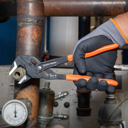 Detail shot of a professional using a Klein Tools compact plier wrench on a brass valve, highlighting the tool's precision and high-torque grip.