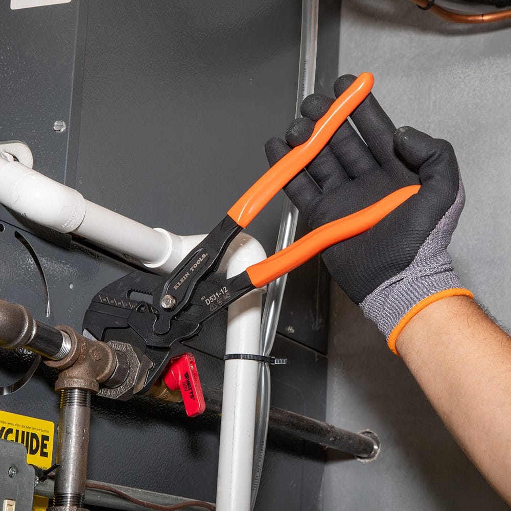 Technician using the 12-inch compact plier wrench from the D53103KIT to adjust a valve on a white PVC pipe system near an HVAC unit.