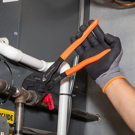 Technician using the 12-inch compact plier wrench from the D53103KIT to adjust a valve on a white PVC pipe system near an HVAC unit.