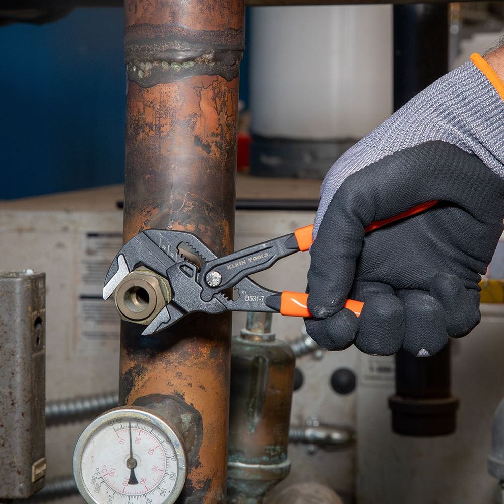Detail shot of a professional using the 7-inch Klein Tools compact plier wrench on a copper pipe fitting, highlighting the tool's non-marring smooth jaws and secure grip.