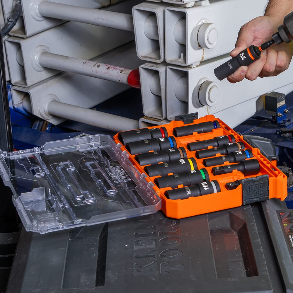 Technician attaching a Klein 9/16-inch deep impact socket to a power tool next to an open MODbox kit on a jobsite scissor lift.