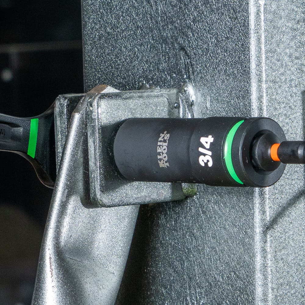 Contractor using a Klein 3/4-inch deep-well impact socket with a 1/4-inch quick-connect adapter to tighten structural machinery bolts.