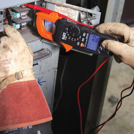 Electrician working on wiring inside a metal stud wall, wearing PPE and using tools near a junction box with green, white, and red wires.