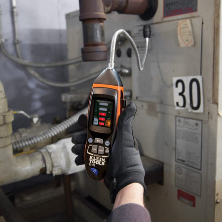 A technician troubleshooting a commercial HVAC unit using the ET120 gas leak detector. The flexible probe is reaching into the internal mechanical components to verify the integrity of the gas valves and fittings.