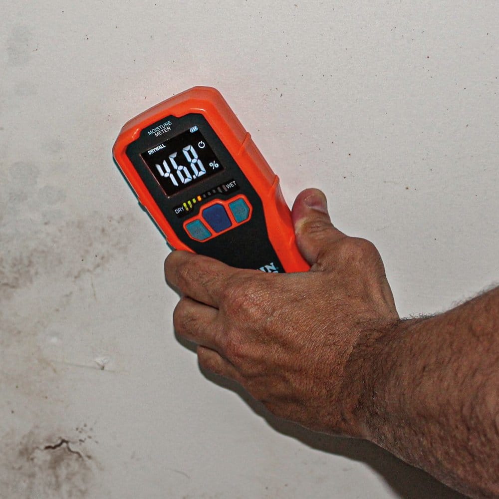 Action photo showing a person using the ET140 moisture meter to scan a drywall surface. The screen displays a 46.8 percent reading with the yellow and red LED bars on the graph indicating elevated moisture levels.