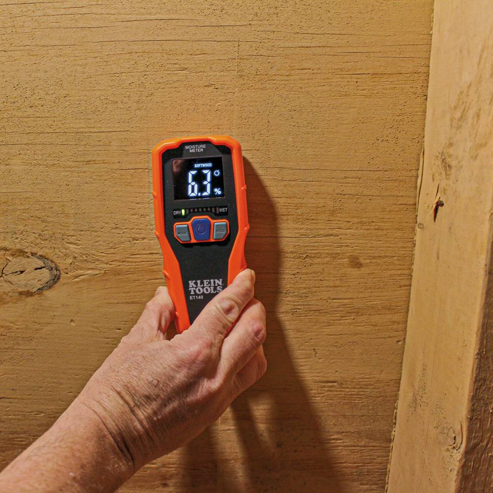 A close-up photo of the ET140 moisture meter being used on a wooden surface. The device is set to softwood mode and displays a relative moisture reading of 6.3 percent with green LED bars on the graph.