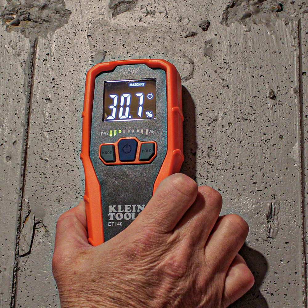 Action shot of the ET140 moisture meter being pressed against a concrete wall. The device is set to masonry mode and displays a 30.7 percent relative moisture reading with yellow LED bars illuminated.